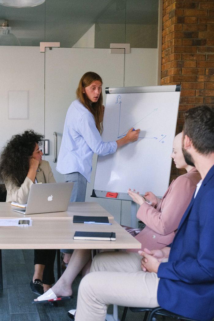 about-us-02 Pensive employee in formal clothes drawing graph on flipchart while explaining project to coworkers during seminar in workspace in daytime